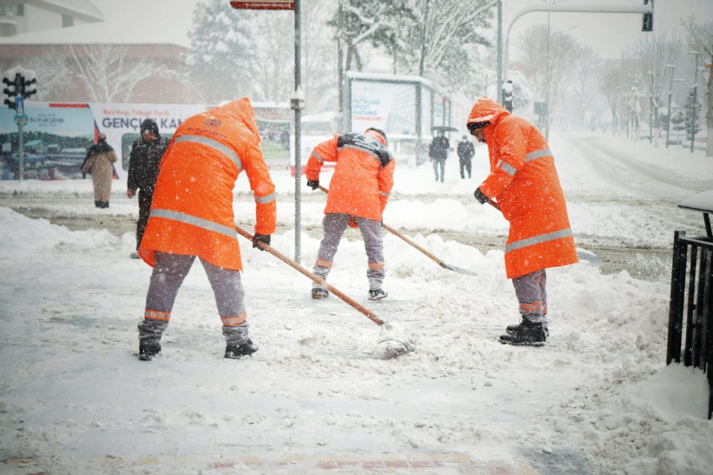 Arbeiter in orangefarbenen Uniformen räumen schweren Schnee auf einer Straße in Malatya, Türkei.