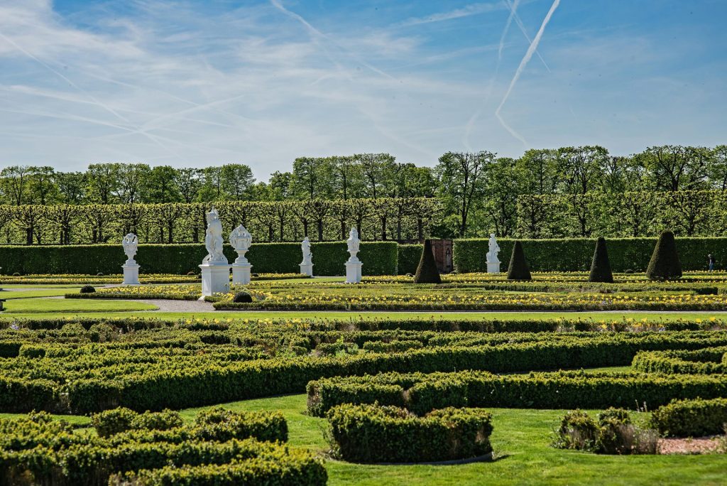 Ein wunderschön gepflegter Garten mit weißen Skulpturen und getrimmten Hecken unter einem klaren blauen Himmel in Hannover.